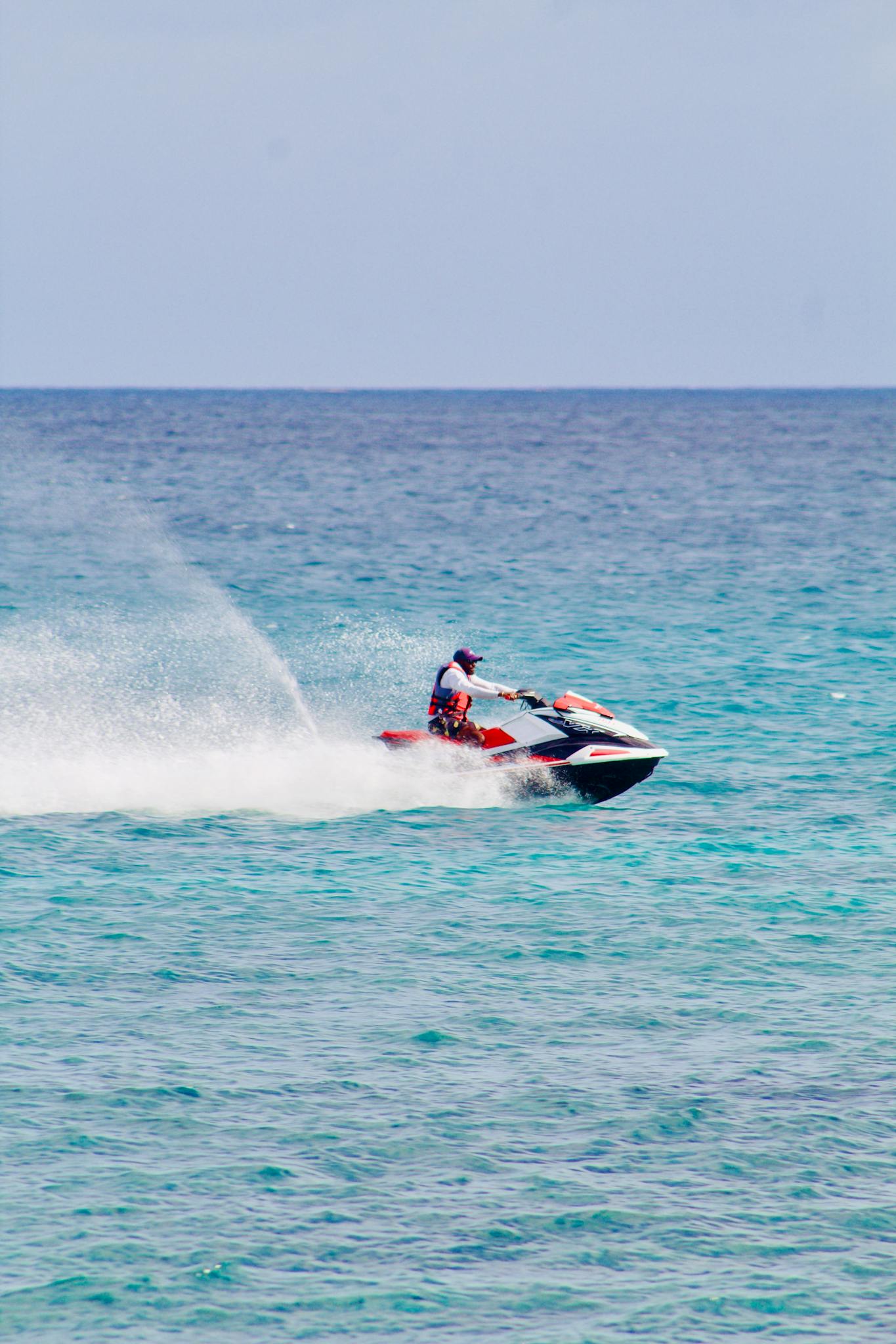 Action shot of a man enjoying jet skiing on clear, blue ocean waters under a sunny sky.